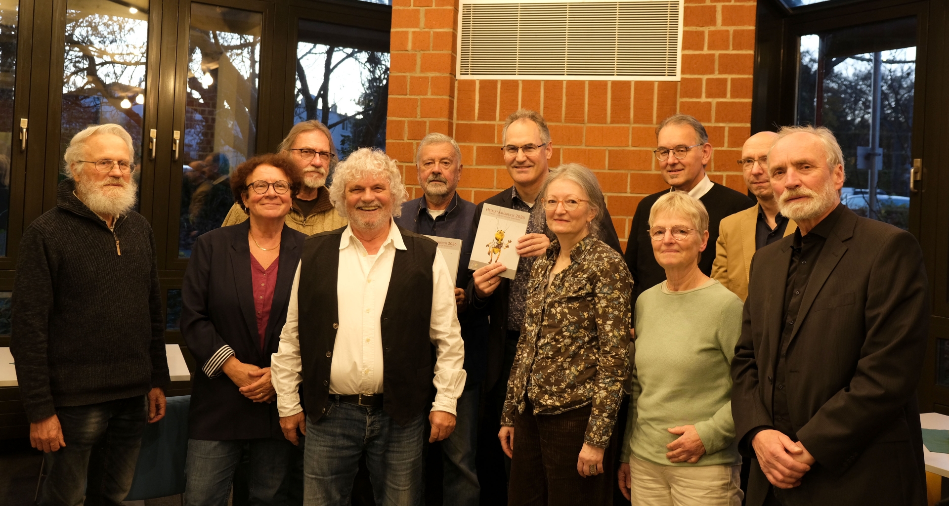 Elf Personen vor Backsteinmauer und Fensterfront.