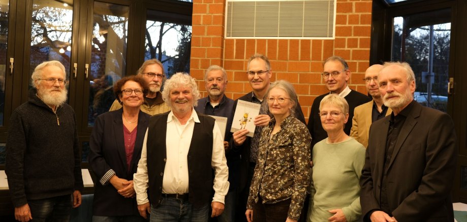 Elf Personen vor Backsteinmauer und Fensterfront.