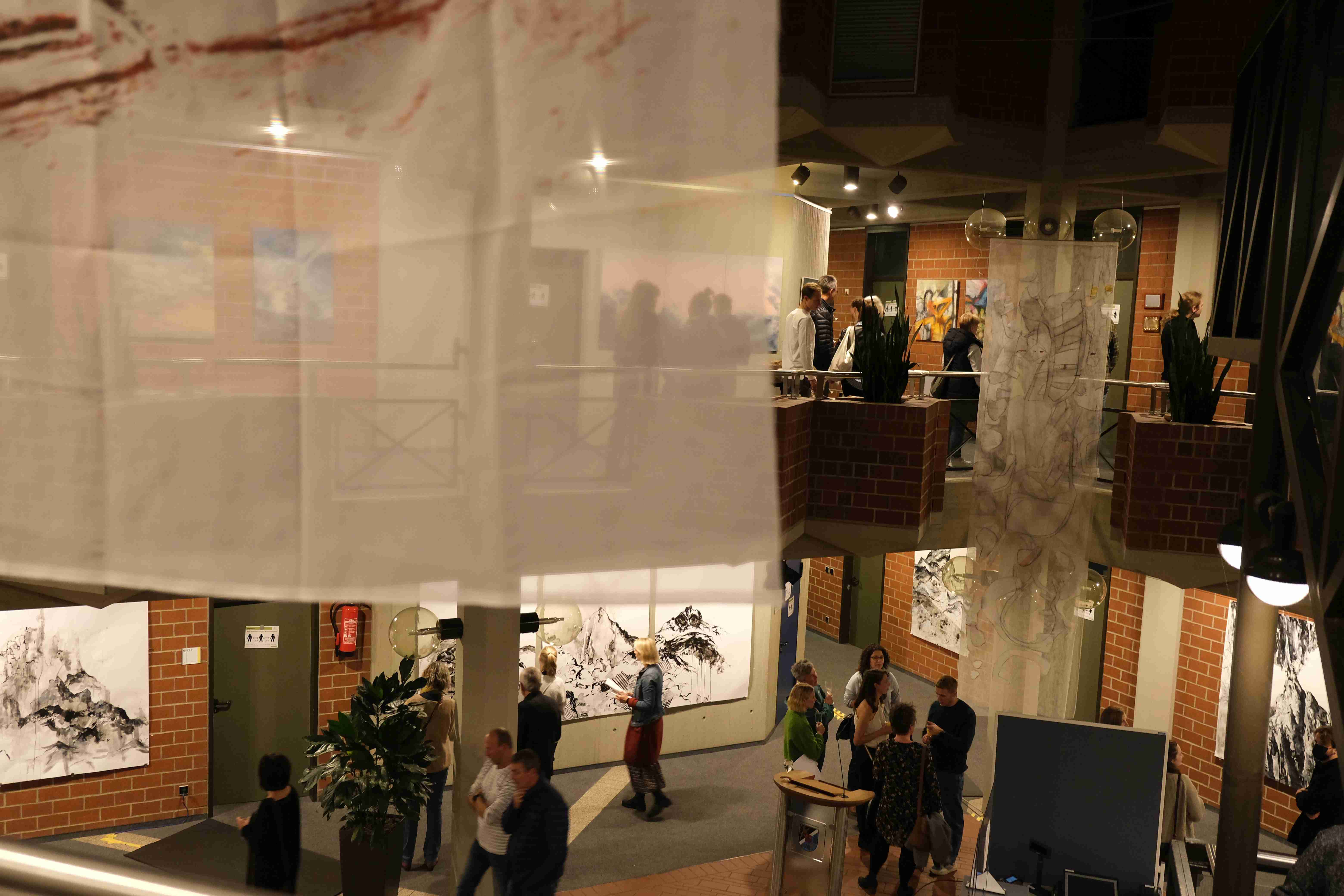 Ausstellungseröffnungen gehören in den Jahreskalender des Kreishauses SÜW. Foto: KV SÜW Menschen auf zwei Stockwerken im Kreishaus betrachten Kunstwerke.