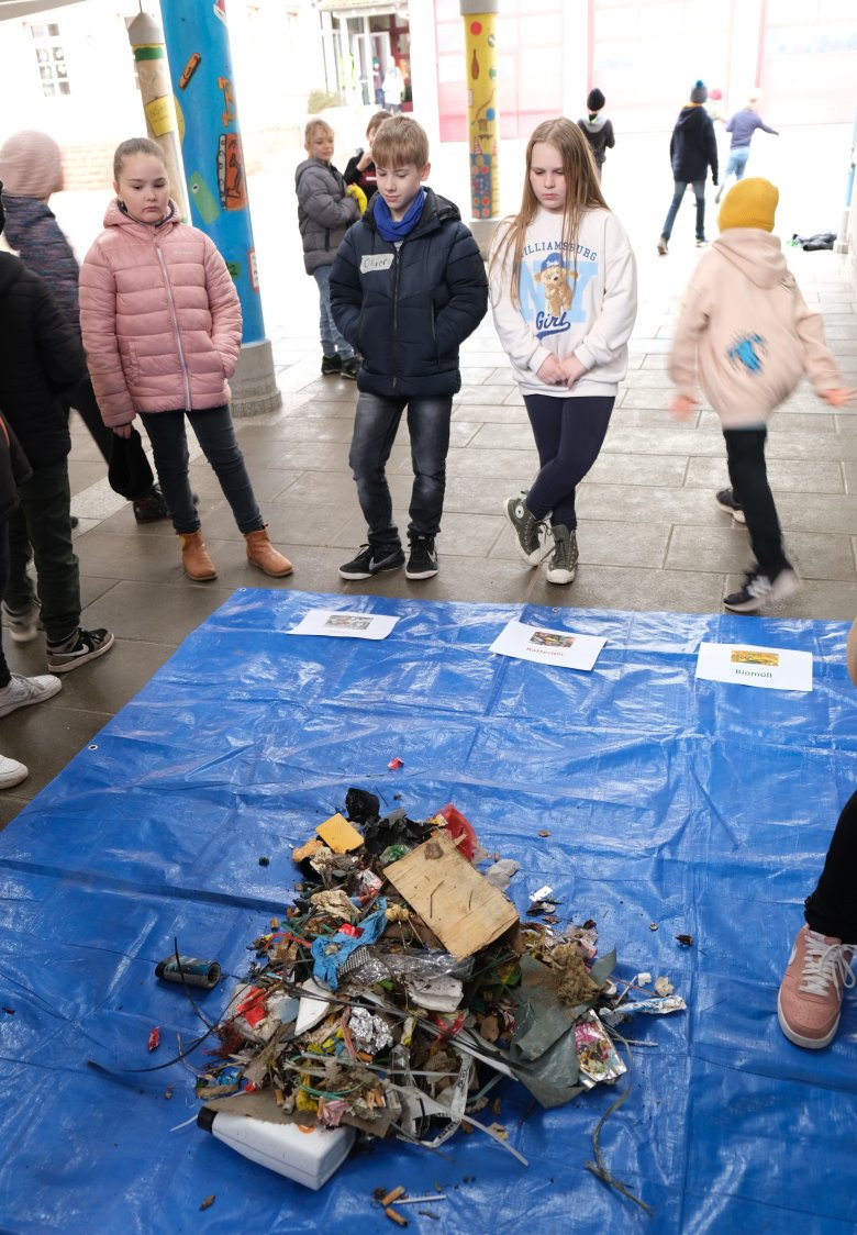 Das „Sammelergebnis“ im Schulhof Insheim. Foto: KV SÜW Müll auf einer blauen Plan wird von Kindern betrachtet.