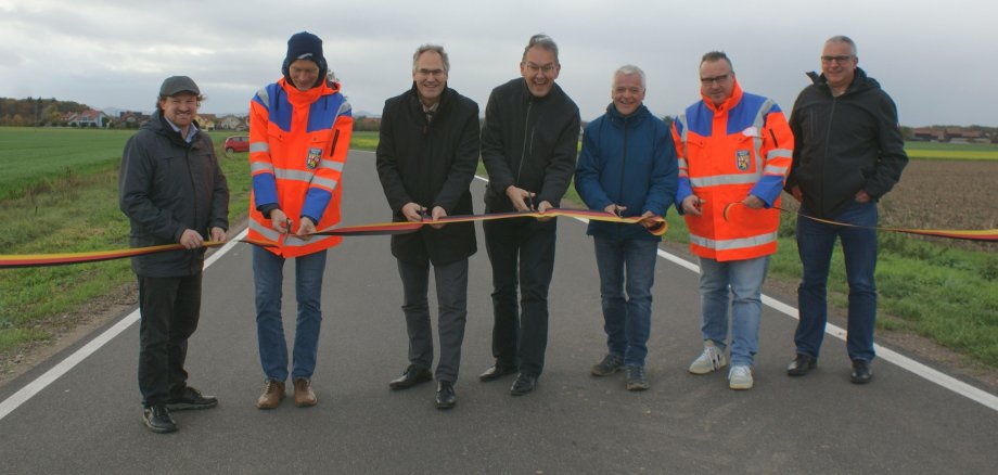 Sieben Männer in Funktion stehen auf der Kreisstraße 62 zwischen Hayna und Hatzenbühl und zerschneiden mit Scheren ein gespanntes Band.