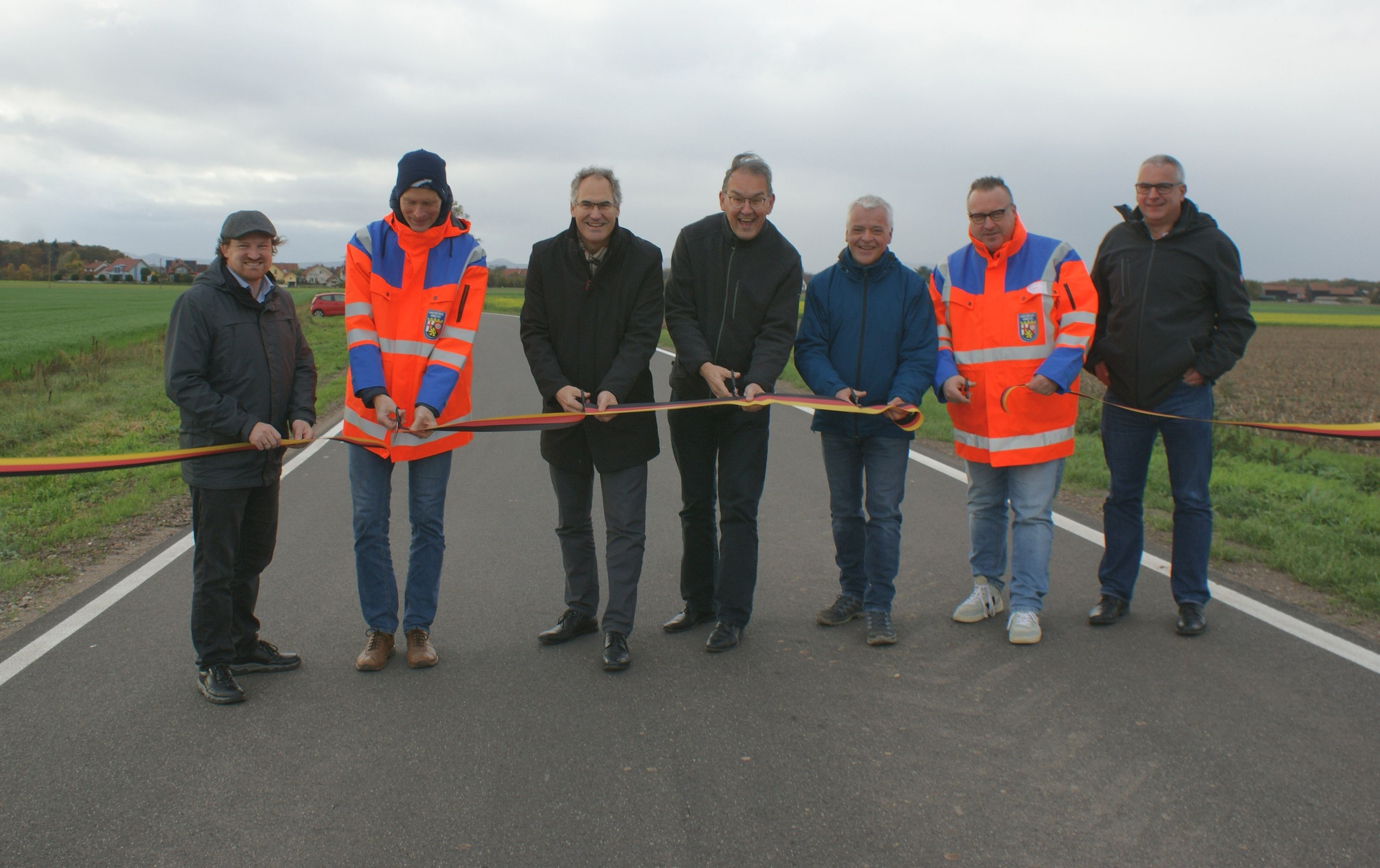 Sieben Männer in Funktion stehen auf der Kreisstraße 62 zwischen Hayna und Hatzenbühl und zerschneiden mit Scheren ein gespanntes Band.