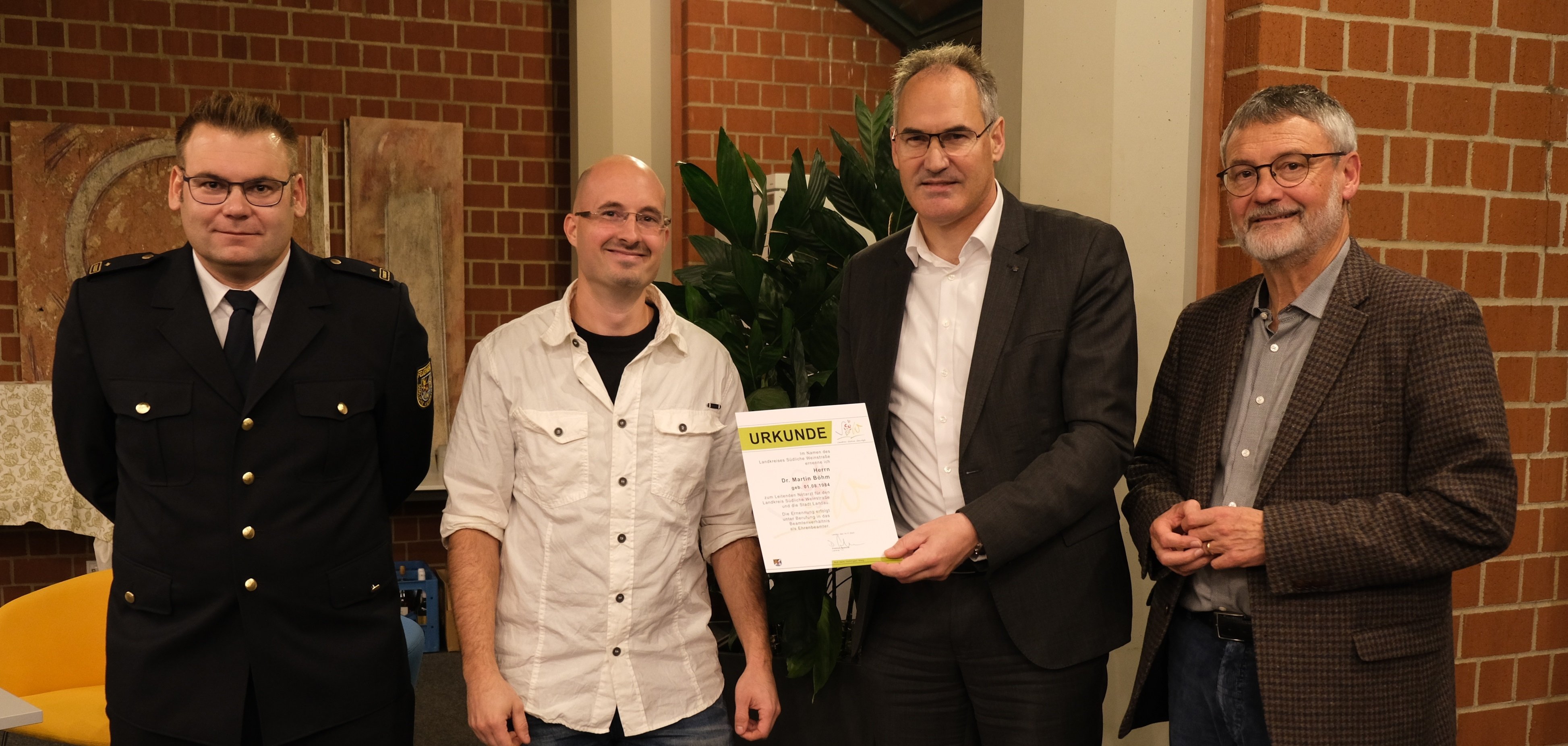 Brand- und Katastrophenschutzinspekteur der Südlichen Weinstraße Jens Thiele, Dr. Martin Böhm, Landrat Dietmar Seefeldt und Kreisbeigeordneter Kurt Wagenführer stehen in einer Reihe, Landrat Seefeldt überreicht Dr. Böhm die Ernennungsurkunde zum Leitenden Notarzt.