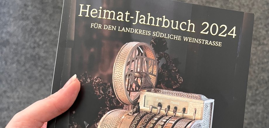 Eine Hand hält das Heimatjahrbuch, auf dessen Titel eine alte Kasse zu sehen ist. 