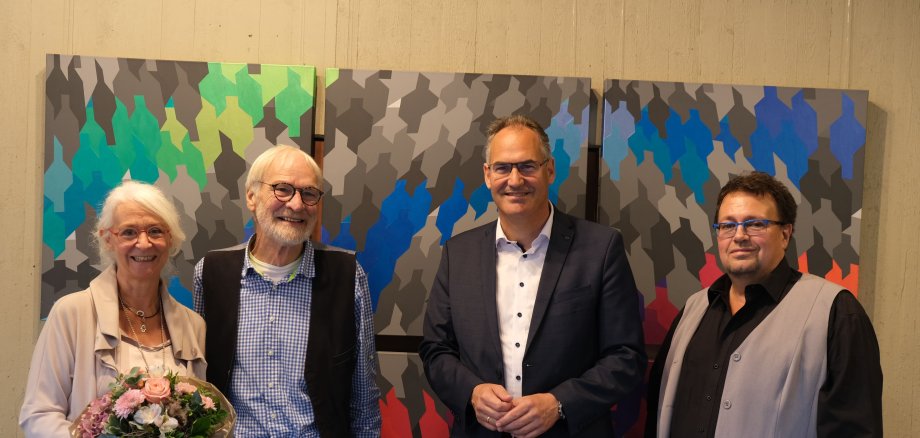 Fünf Personen stehen vor einem großflächigen, bunten Kunstwerk aus geoemetrischen Figuren. 