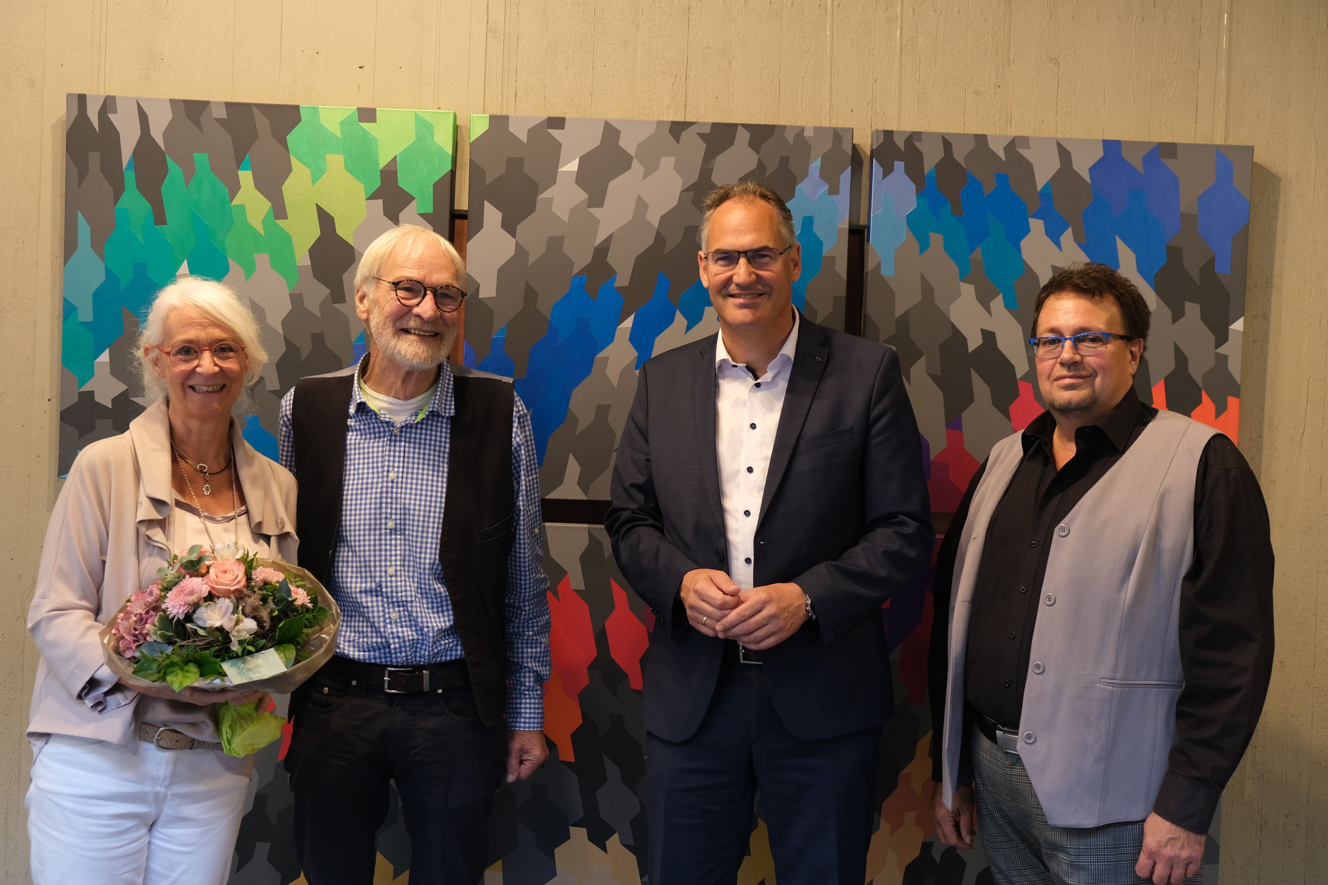 Fünf Personen stehen vor einem großflächigen, bunten Kunstwerk aus geoemetrischen Figuren. 