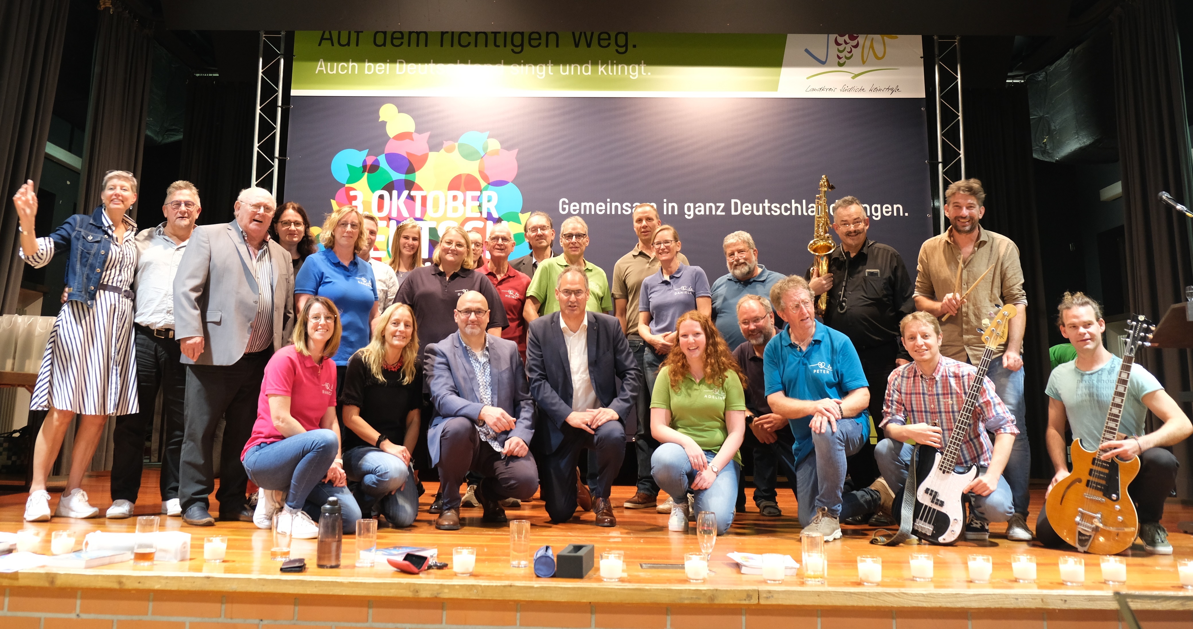 Eine große Gruppe fröhlicher Menschen steht vor einer Wand mit der Aufschrift "Deutschland singt und klingt". 