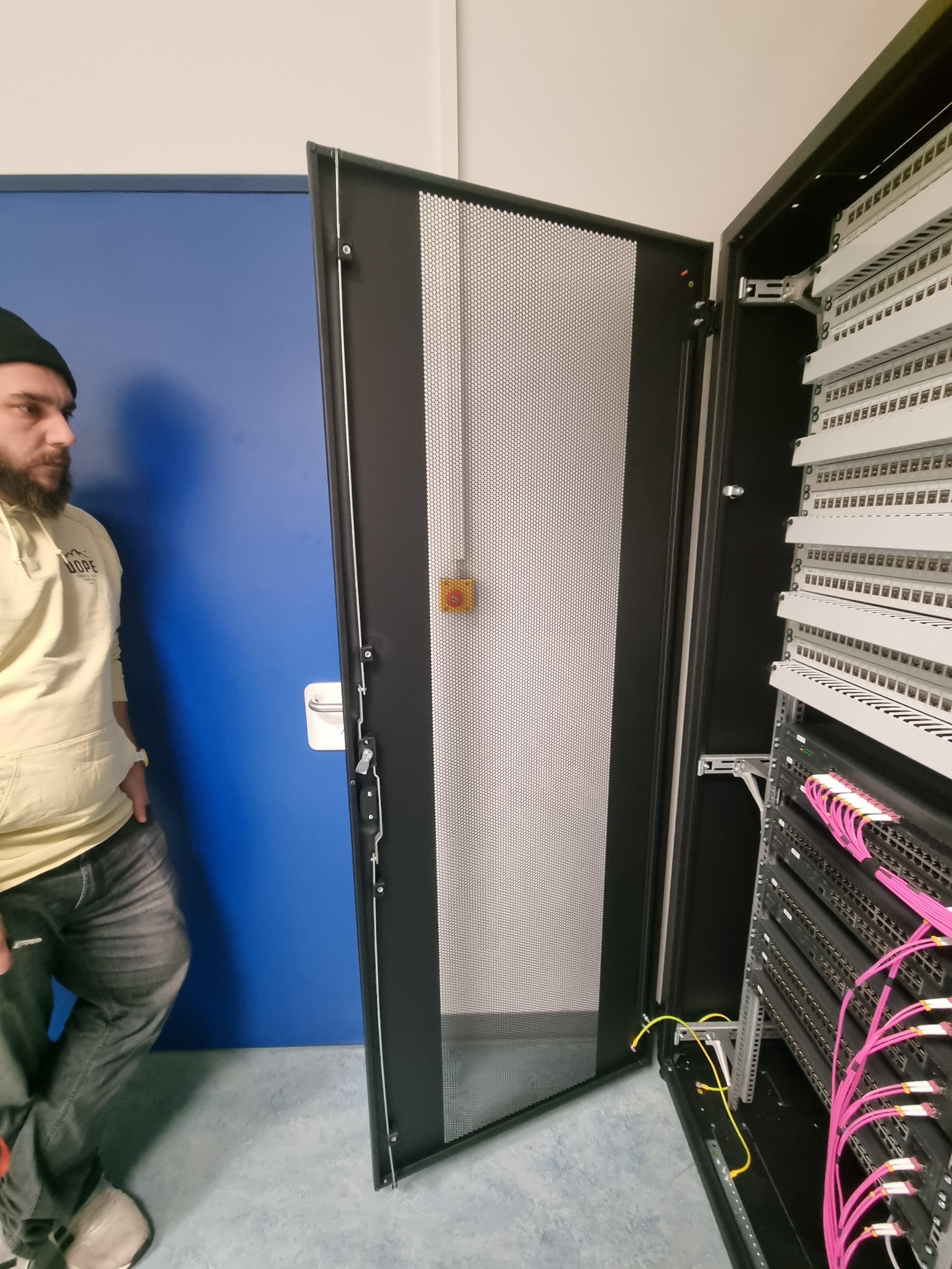 Eine männliche Person steht neben einem geöffneten Netzwerk-Schrank.