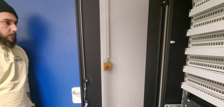 Eine männliche Person steht neben einem geöffneten Netzwerk-Schrank.