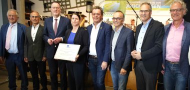 Prof. Dr. Christoph Wulf, Vizepräsident der Deutschen UNESCO-Kommission, Pirmin Hilsendegen (IG Queichwiesen), Minister Michael Ebling, Friederike Hansell, Beauftragte der Kultusministerkonferenz für das Unesco-Welterbe, Bürgermeister Gerald Job, Landrat Dr. Fritz Brechtel (Germersheim), Landrat Dietmar Seefeldt (Südliche Weinstraße), Axel Wassyl, Bürgermeister der Verbandsgemeinde Offenbach, stehen beim Festakt in einer Reihe. Foto: KV Germersheim