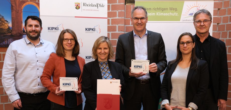 Klimaschutzministerin Katrin Eder (Dritte von links) überreichte Landrat Dietmar Seefeldt (Dritter von rechts) im Kreishaus in Landau den KIPKI-Förderbescheid. Mit im Bild (von links): Steven Barth, Referatsleiter des Zentralen Gebäudemanagements der Kreisverwaltung SÜW, Landtagsabgeordnete Lea Heidbreder, SÜW-Klimaschutzmanagerin Fabienne De Pasquale und Günter Jung, Leiter der Abteilung Bauen und Umwelt der Kreisverwaltung. Foto: KV SÜW