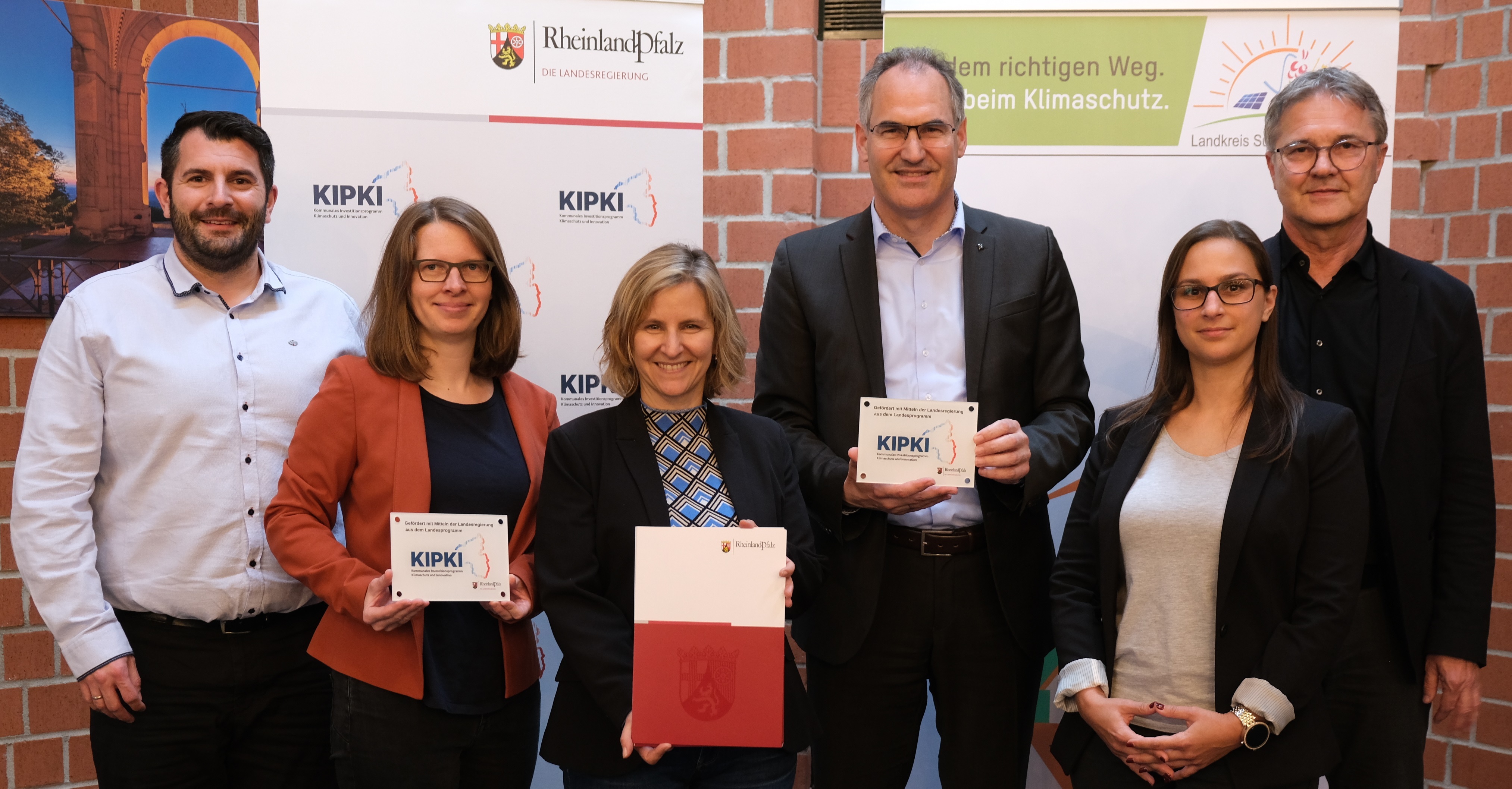 Klimaschutzministerin Katrin Eder (Dritte von links) überreichte Landrat Dietmar Seefeldt (Dritter von rechts) im Kreishaus in Landau den KIPKI-Förderbescheid. Mit im Bild (von links): Steven Barth, Referatsleiter des Zentralen Gebäudemanagements der Kreisverwaltung SÜW, Landtagsabgeordnete Lea Heidbreder, SÜW-Klimaschutzmanagerin Fabienne De Pasquale und Günter Jung, Leiter der Abteilung Bauen und Umwelt der Kreisverwaltung. Foto: KV SÜW