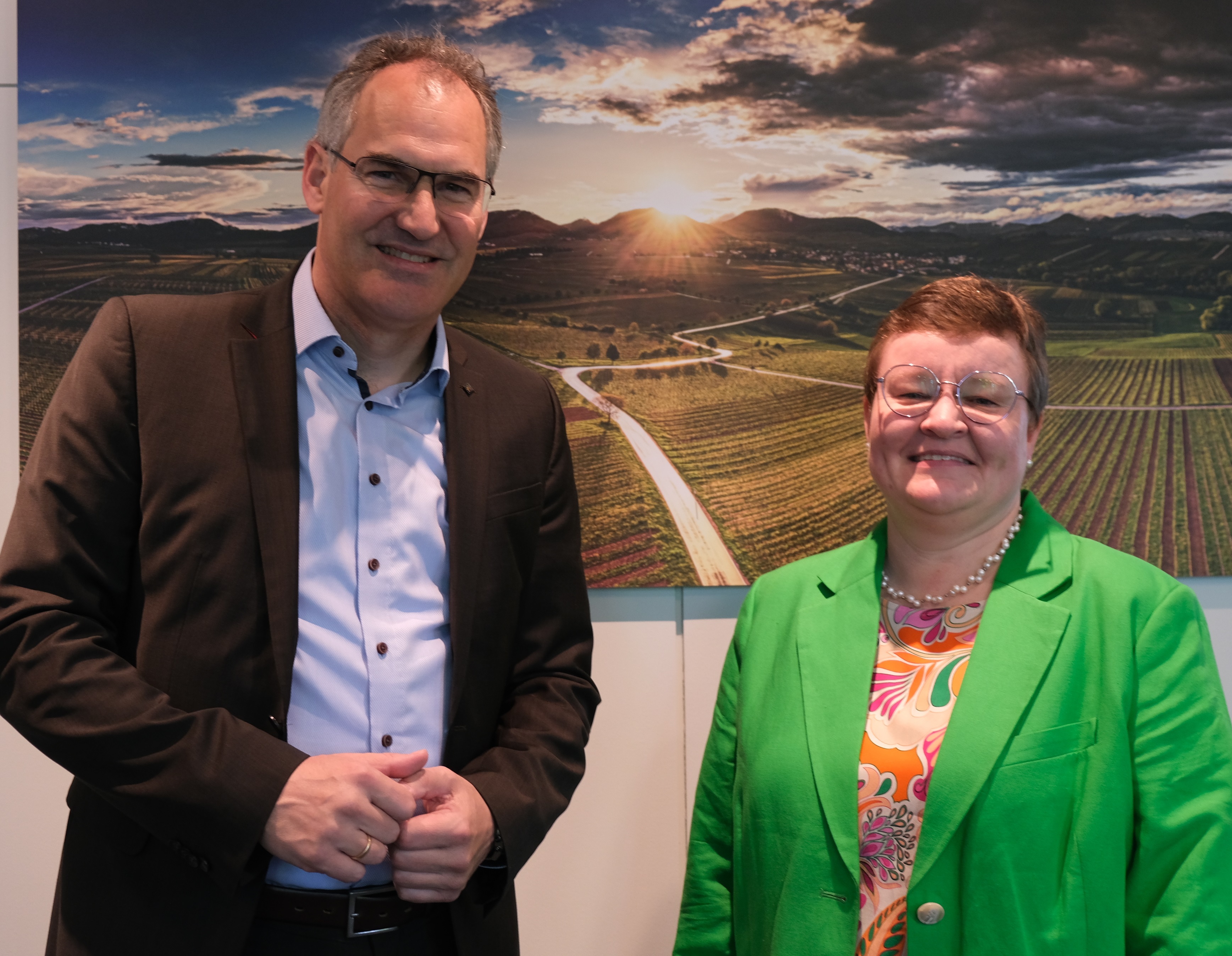 Landrat Dietmar Seefeldt und die neue Leitende staatliche Beamtin Sarina Hildmann stehen vor einem Landschaftsbild im Kreishaus.
