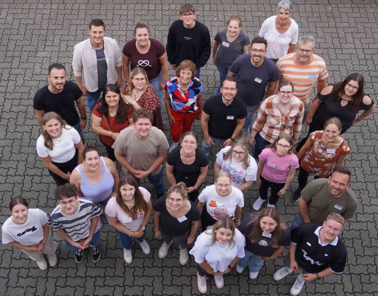 Gruppenfoto von Teilnehmern des Azubi-Tags der Kreisverwaltung. Die Gruppe steht im Freien auf einem gepflasterten Platz und blickt fröhlich nach oben in die Kamera. Die Teilnehmer sind in legerer Kleidung und wirken gut gelaunt.