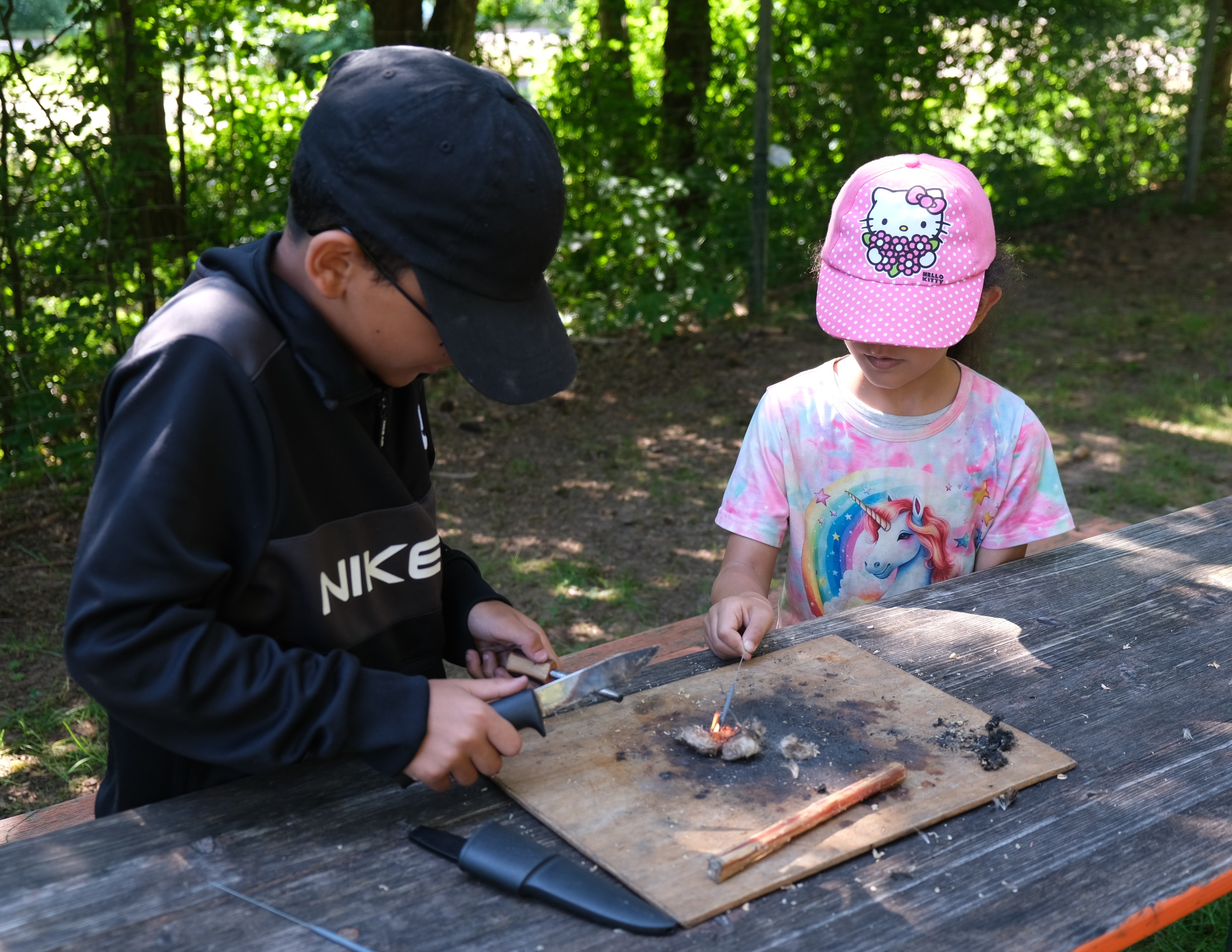 Eine Junge entfacht mit Feuerstein, Kiefernholz und Distelhaar eine Flamme, an der seine Schwester eine Wunderkerze entzündet.
