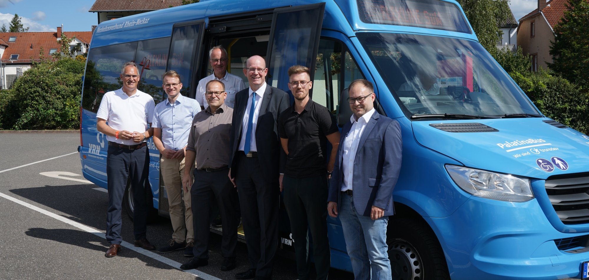 Die Teilnehmer der Premierenfahrt (von links): Landrat Dietmar Seefeldt, Daniel Salm, Bürgermeister der Verbandsgemeinde Edenkoben, Eberhard Frankmann, Erster Beigeordneter der Verbandsgemeinde Edenkoben, Christian Wühl, Abteilungsleiter Planung und Angebot des VRN, Geschäftsführer der Palatina Bus GmbH Marcus Weigl, Benjamin Klar, ÖPNV-Referent des Landkreises SÜW, und Florian Jung, Betriebsleiter der Palatina Bus GmbH. Die Teilnehmer stehen vor dem blauen Kleinbus der VRNflexline.