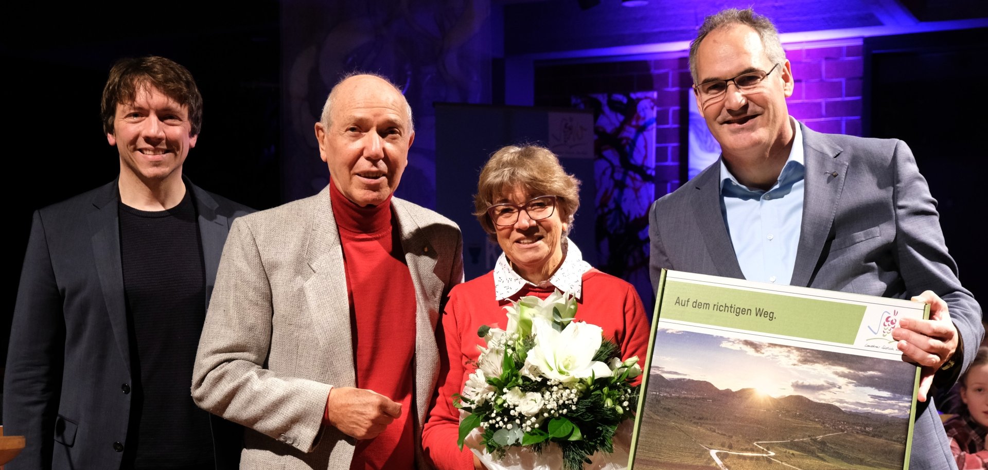 Gruppenbild: Clemens Schmitt erhält im Beisein seiner Frau Sabine Schmitt und Kreismusikschulleiter Adrian Rinck die Goldene Kreiswappennadel von Landrat Dietmar Seefeldt sowie eine SÜW-Box.