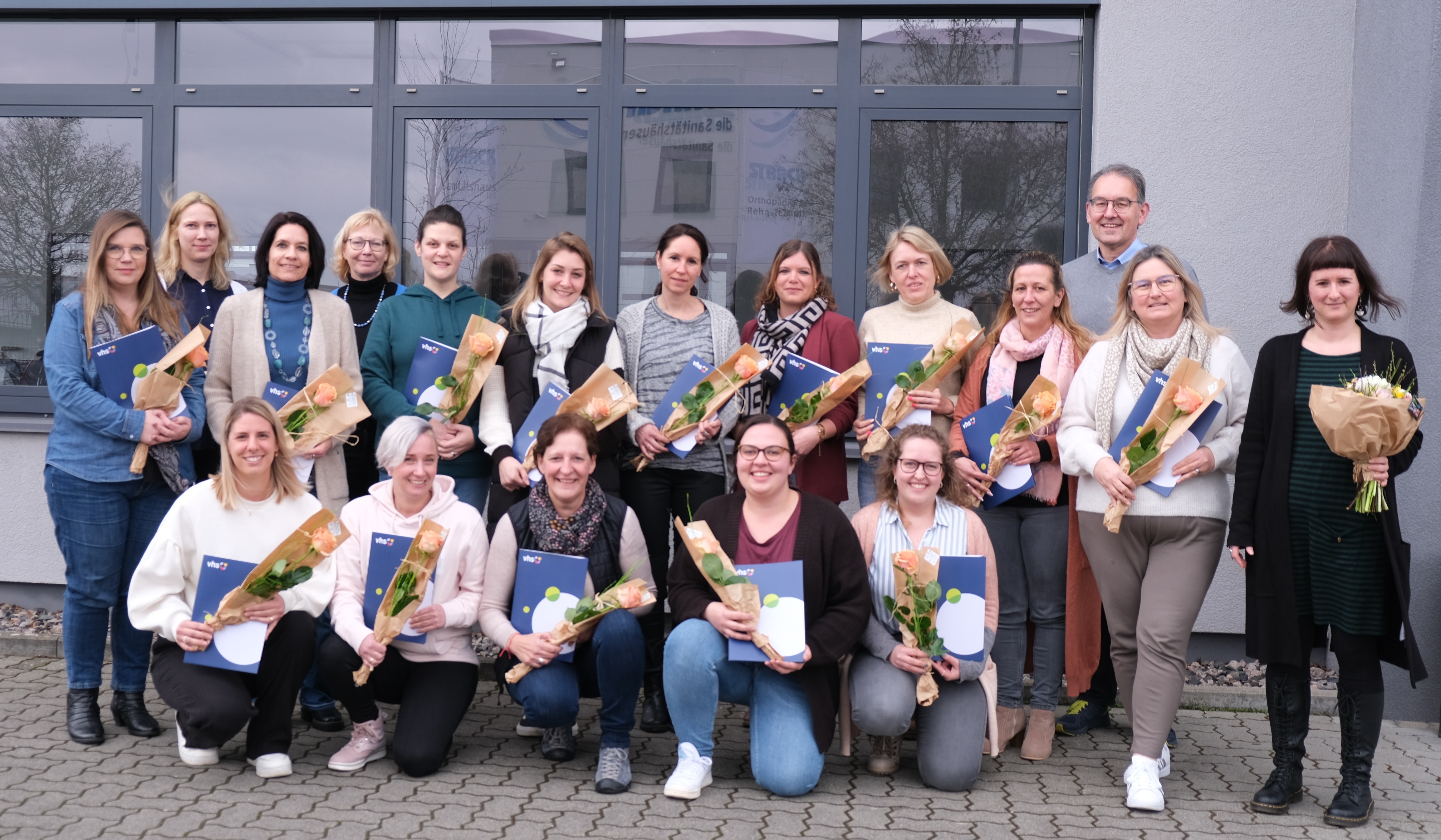 Circa 20 Menschen stehen vor einem Gebäude.