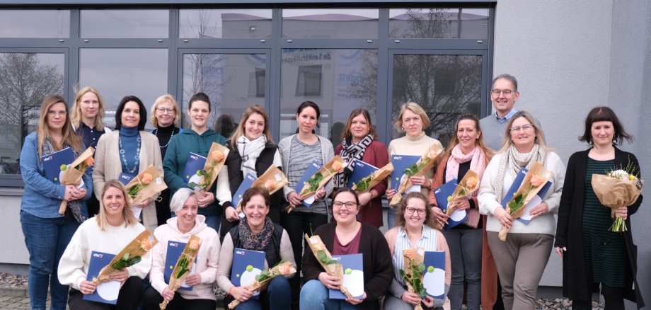 Circa 20 Menschen stehen vor einem Gebäude.