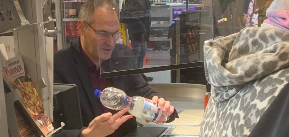 Landrat Dietmar Seefeldt scannt eine Flasche Wasser an einer Supermarkt-Kasse ein.