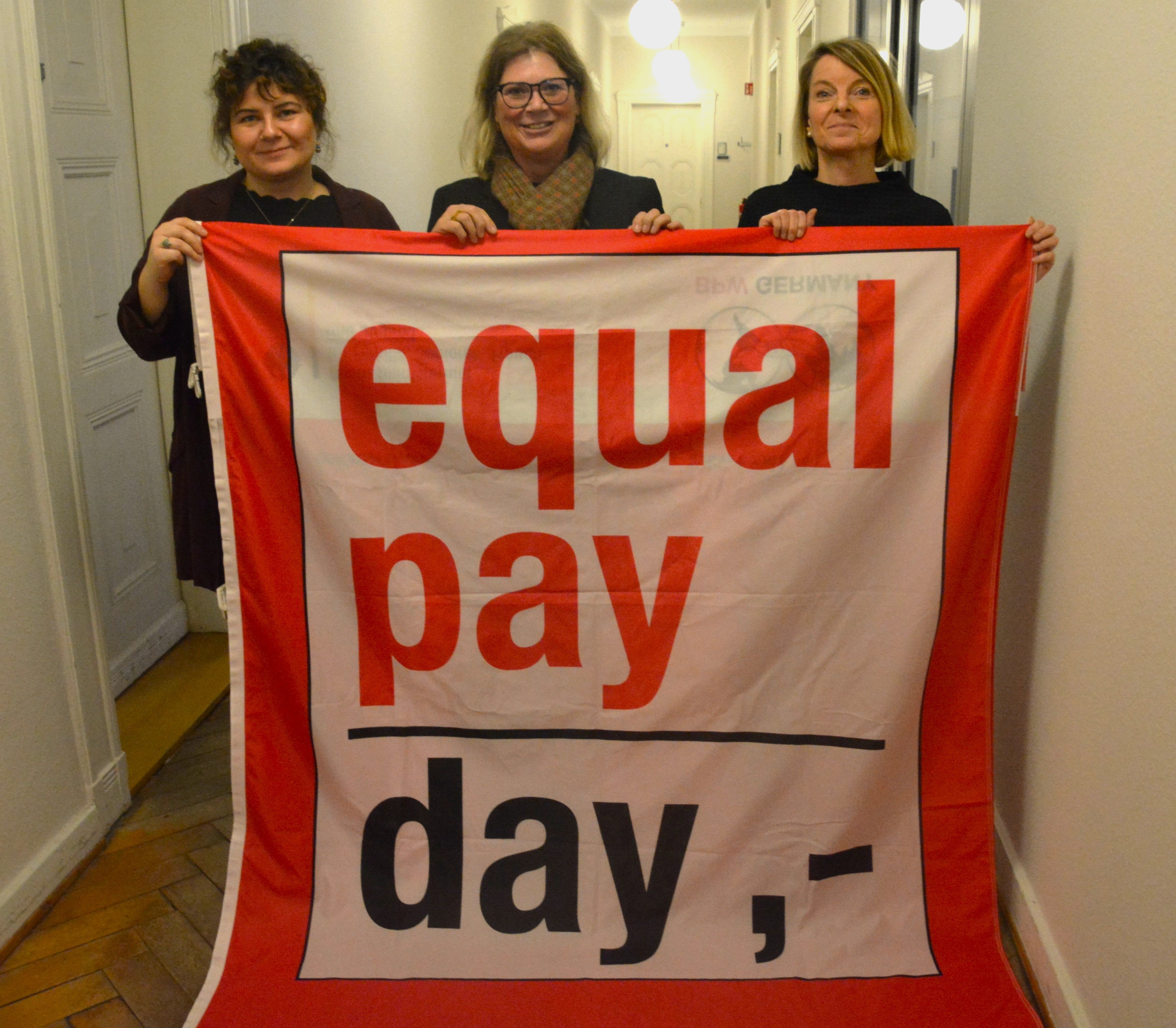 Drei Frauen halten ein rotes Banner hoch. 