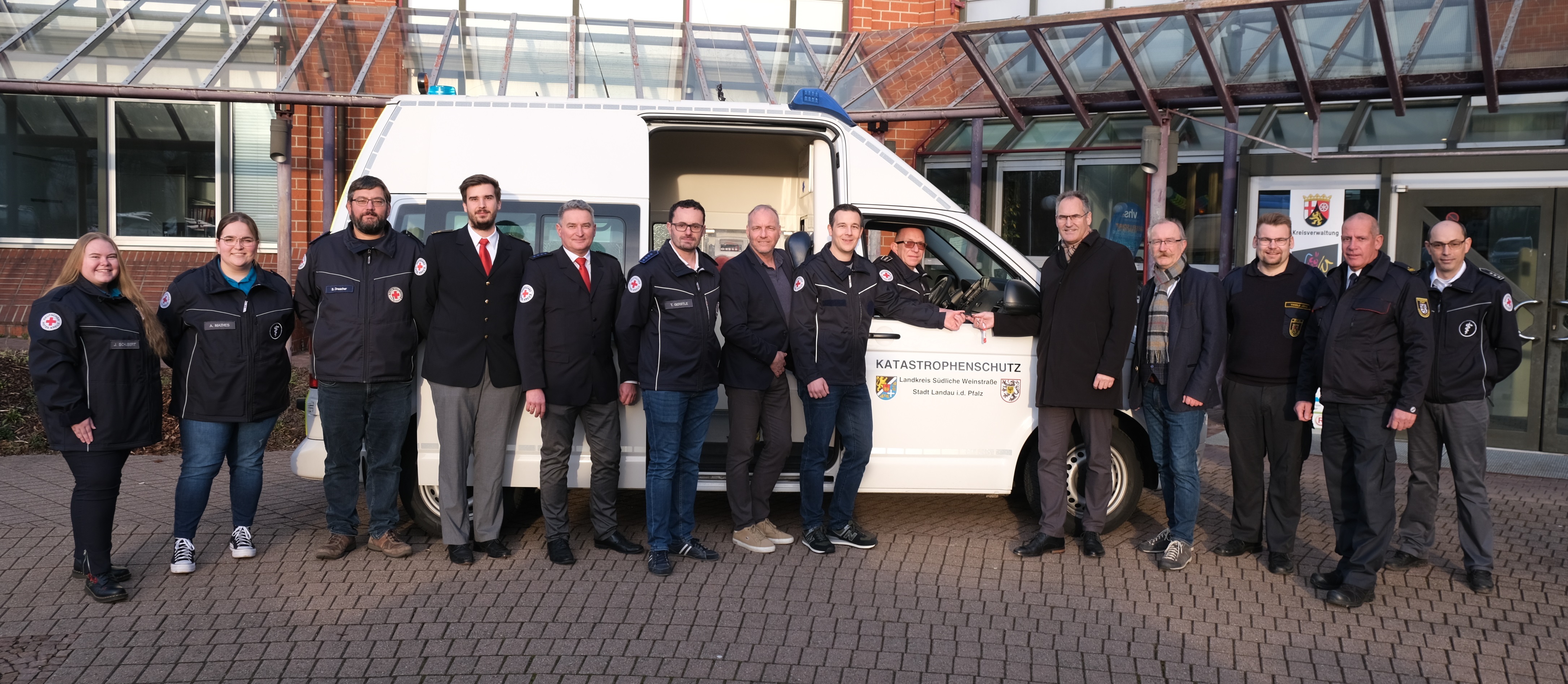 Vertreter der Kreisverwaltung SÜW der Stadt Landau und des DRK Ortsverbands Annweiler am Trifels stehen vor dem neuen weißen Krankentransportwagen. 
