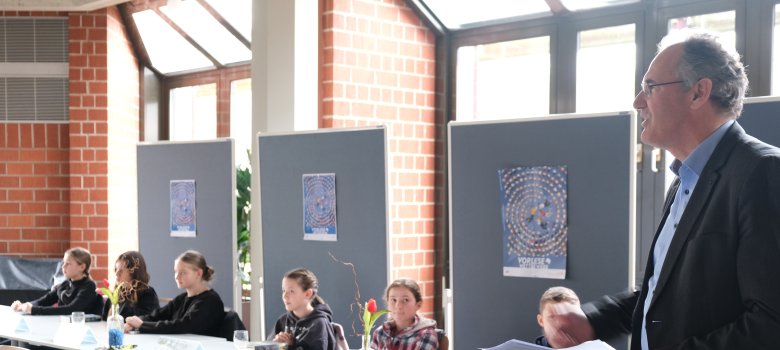 Landrat Dietmar Seefeldt wünschte den sieben Schülerinnen und Schülern viel Glück. Foto: KV SÜW Die Kinder sitzen am Tisch, Landrat Seefeldt steht daneben.