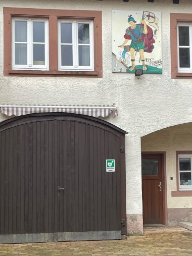 Hinweisschilder, unter anderem auf dem Garagentor des Feuerwehrautos, sollen auf den Standort des AED-Geräts im Dorfgemeinschaftshaus aufmerksam machen. Foto: KV SÜW Hinweisschilder, unter anderem auf dem Garagentor des Feuerwehrautos, sollen auf den Standort des AED-Geräts im Dorfgemeinschaftshaus aufmerksam machen.