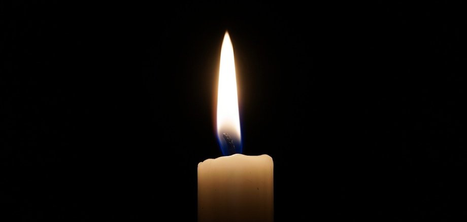 Eine weiße Kerze brennt vor dunklem Hintergrund. 