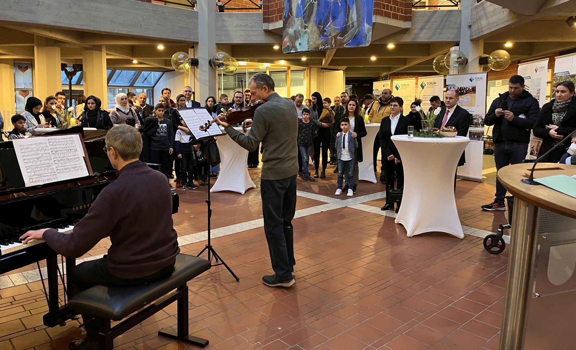Im Vordergrund ein Geige- und ein Violinspieler, im Hintergrund rund 30 Personen bei der Einbürgerungsfeier im Foyer des Kreishauses.