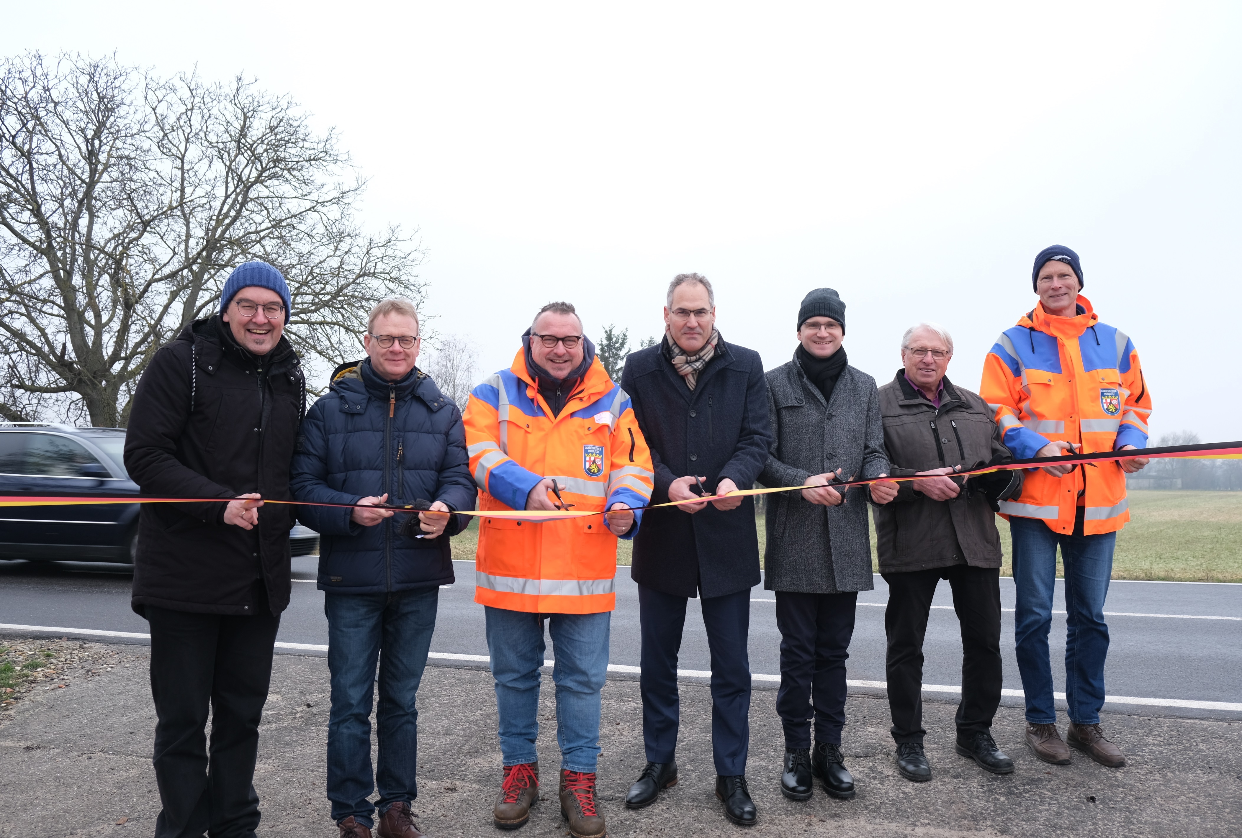 Die Männer stehen an der Straße, im Hintergrund fährt ein Auto. 