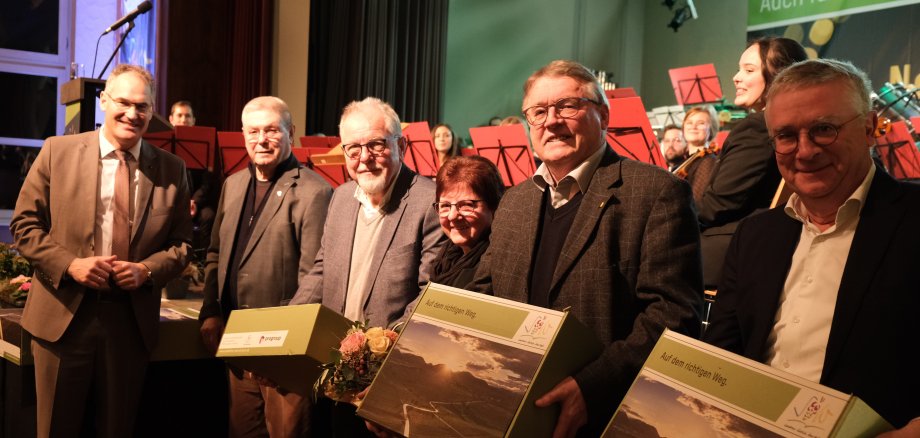 Menschen stehen vor einer Bühne, Geschenkboxen in der Hand. 