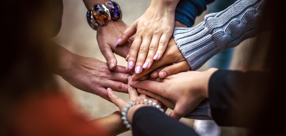 Nahaufnahme von aufeinandergelegten Händen von Menschen verschiedener Hautfarben. 