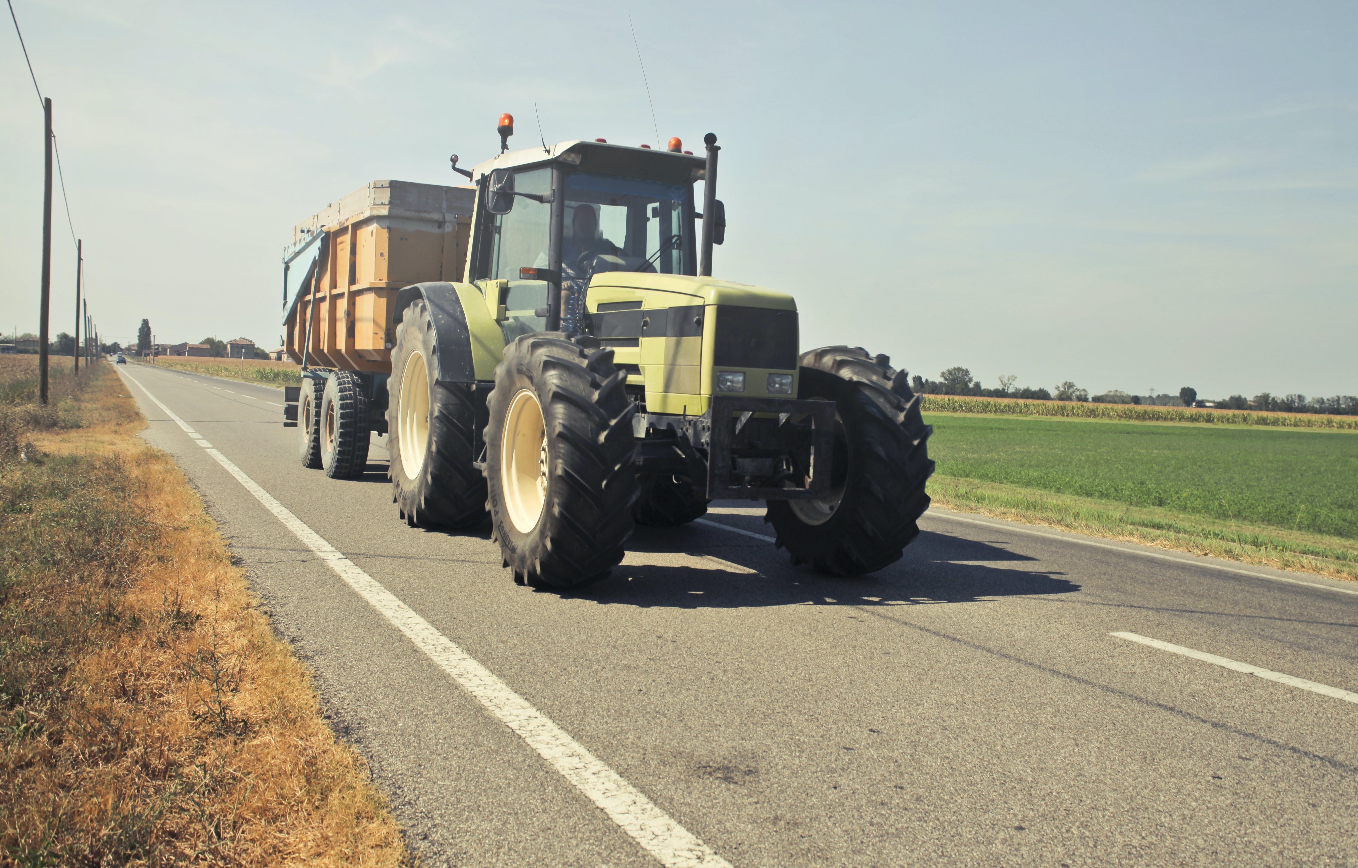 Ein Traktor fährt eine Landstraße entlang. Foto. Pexels