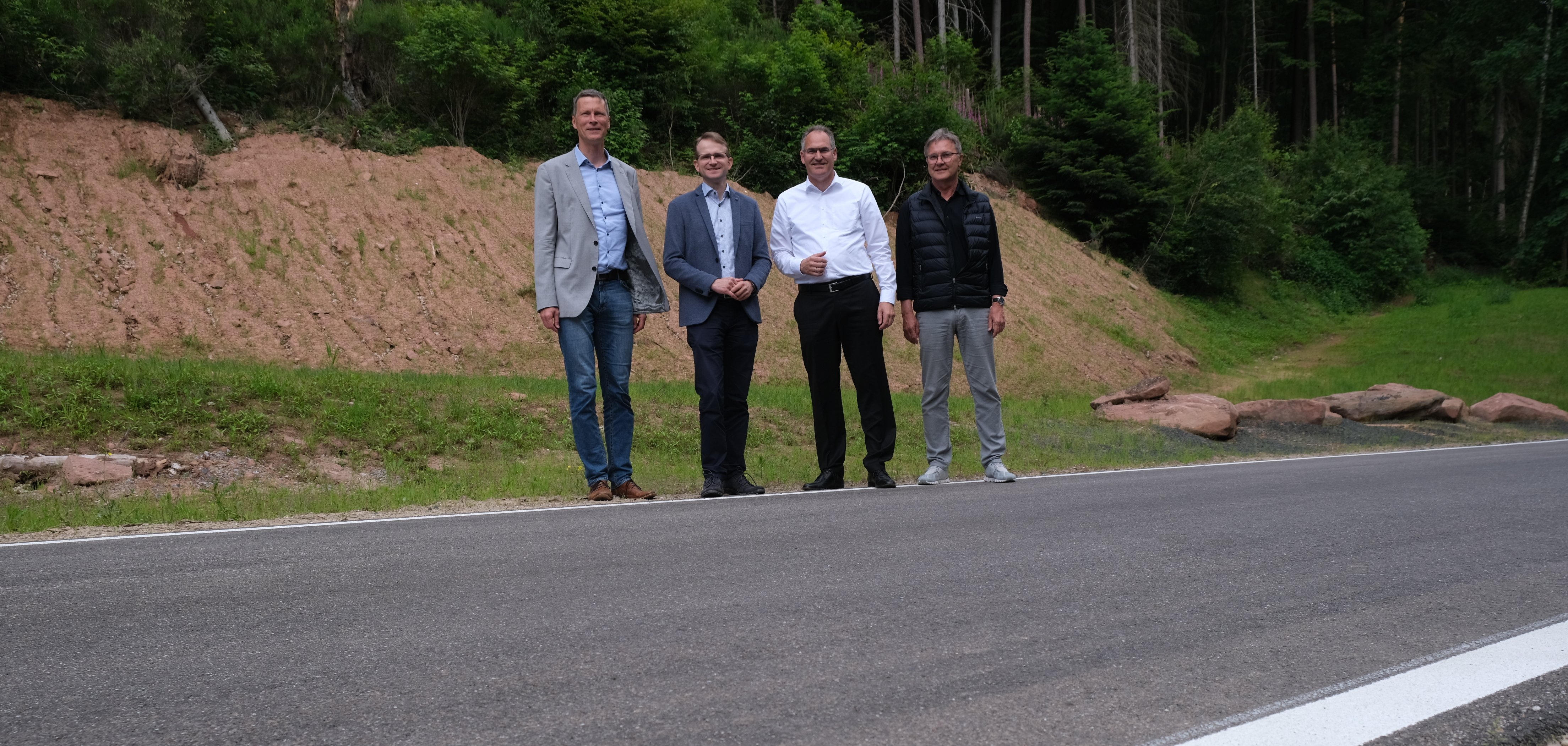 Vier Männer stehen auf einer frisch asphaltierten Straße in ländlicher Umgebung. Sie eröffnen den Abschnitt der Kreisstraße 6 zwischen dem Modenbacher Hof und dem Forsthaus Heldenstein. Von links nach rechts: LBM-Leiter Martin Schafft, Bürgermeister Daniel Salm, Landrat Dietmar Seefeldt und Günter Jung, Leiter der Abteilung Bauen und Umwelt der Kreisverwaltung.