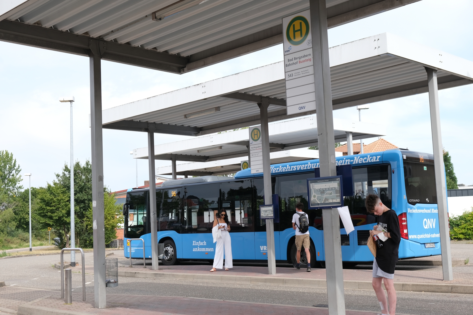 Ein blauer Bus am Busbahnhof, davor wartende Fahrgäste.