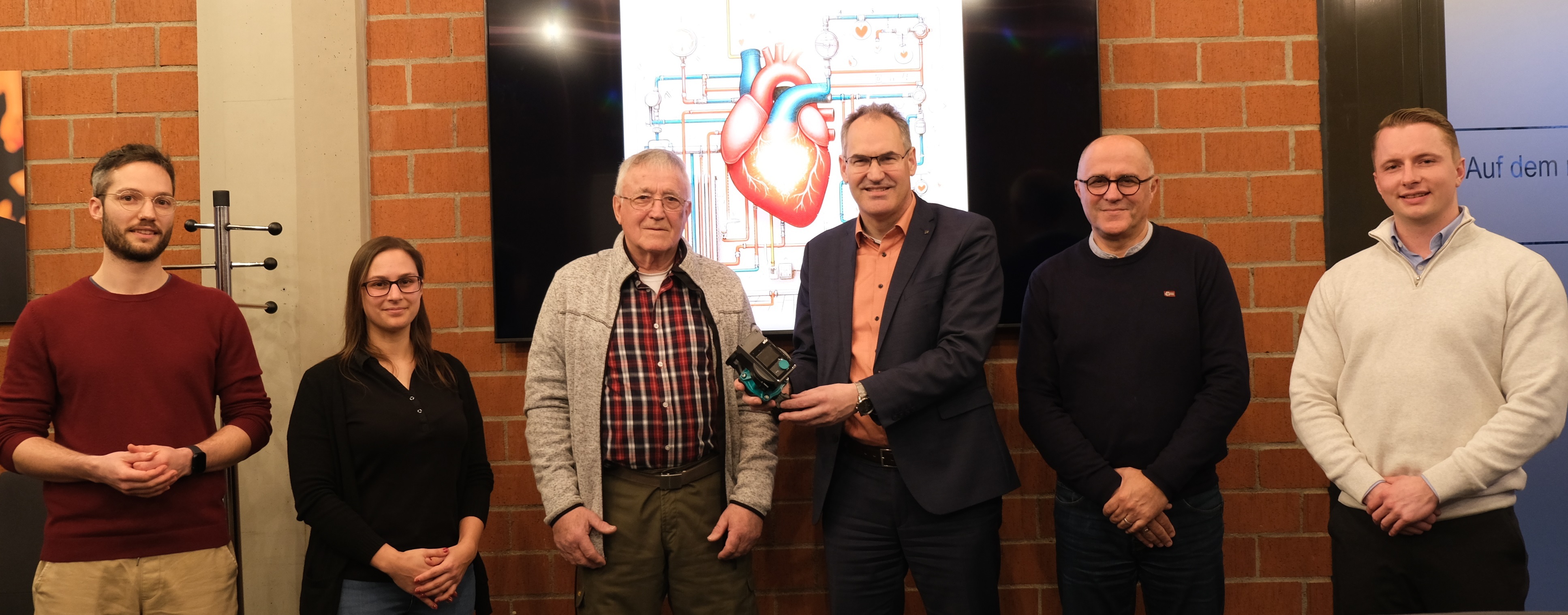 Landrat Dietmar Seefeldt übergibt Florian Hammer im Kreishaus die neue Heizungspumpe. Bei der Übergabe dabei sind außerdem die SÜW-Klimaschutzmanager Philipp Steiner und Fabienne De Pasquale sowie Amar Rezzoug und Jan Augustin von der Haag GmbH in Landau.