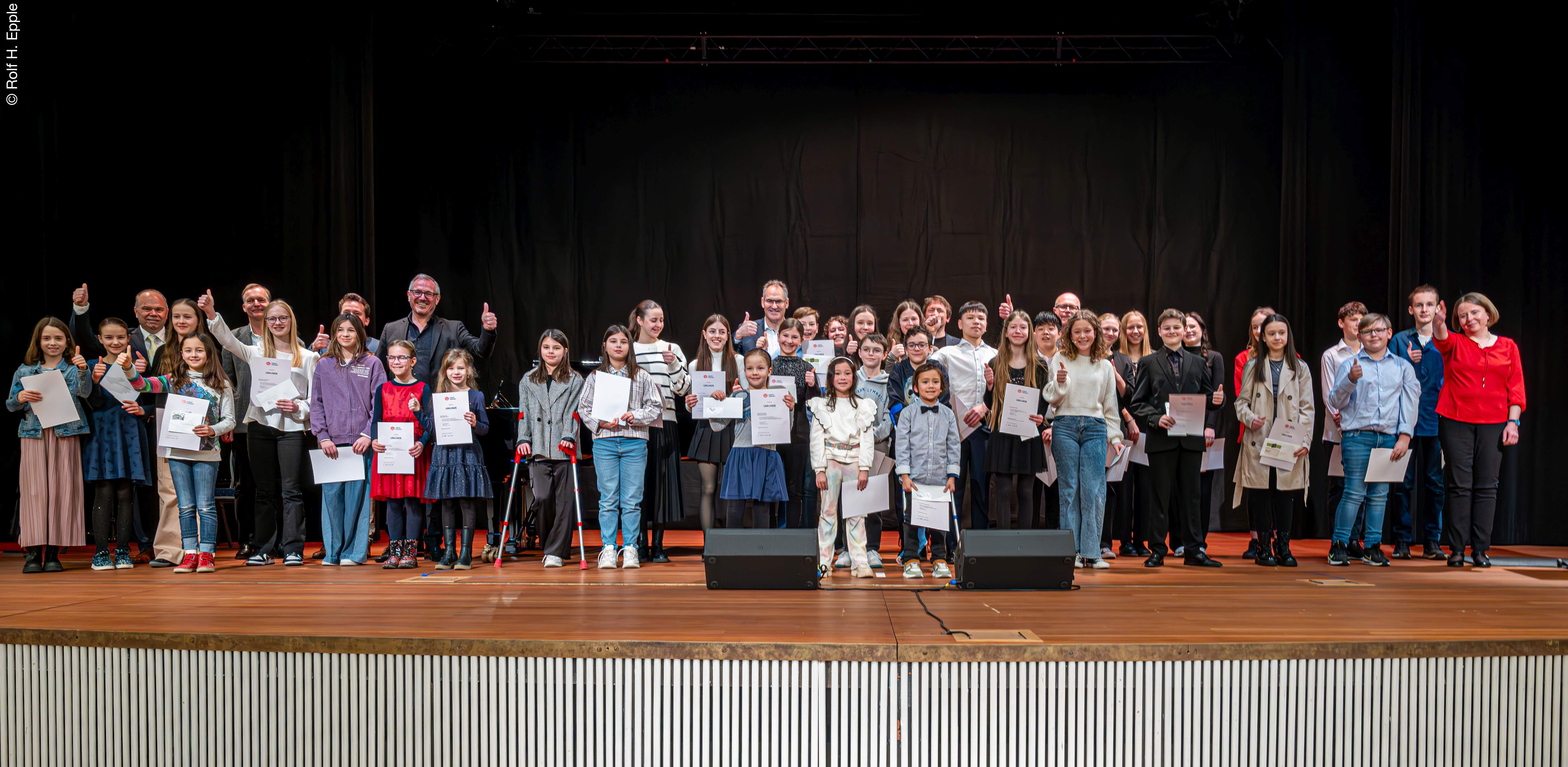 Viele Jugendliche mit Urkunden in der Hand sowie erwachsene Gratulanten stehen auf einer Bühne und recken die Daumen in die Höhe.