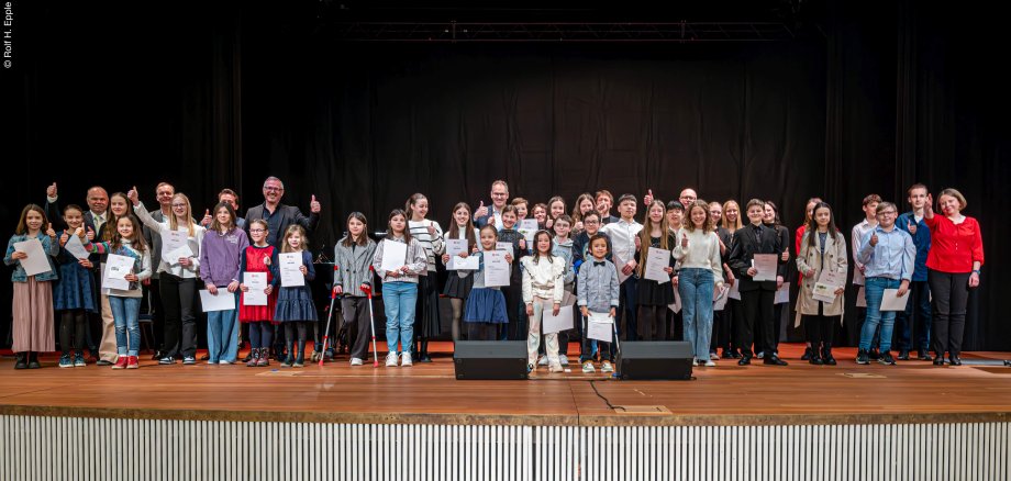 Viele Jugendliche mit Urkunden in der Hand sowie erwachsene Gratulanten stehen auf einer Bühne und recken die Daumen in die Höhe.