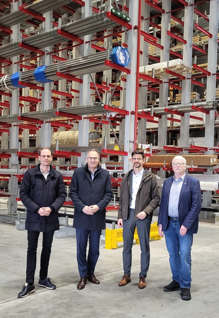 Vier Männer stehen vor Hochregalen.