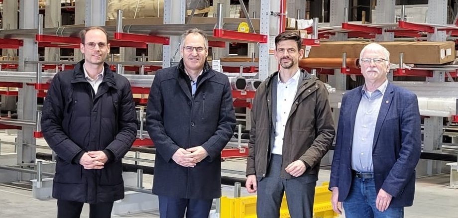 Vier Männer stehen vor Hochregalen.