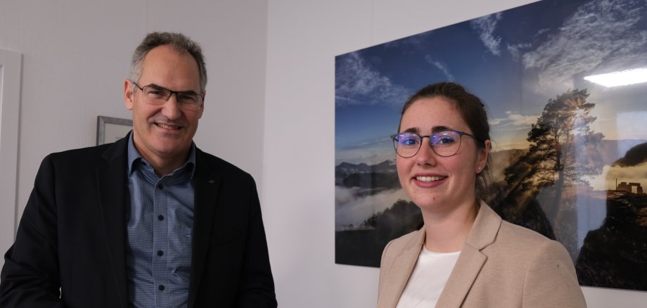 Zwei Personen stehen vor einem Landschaftbiild.