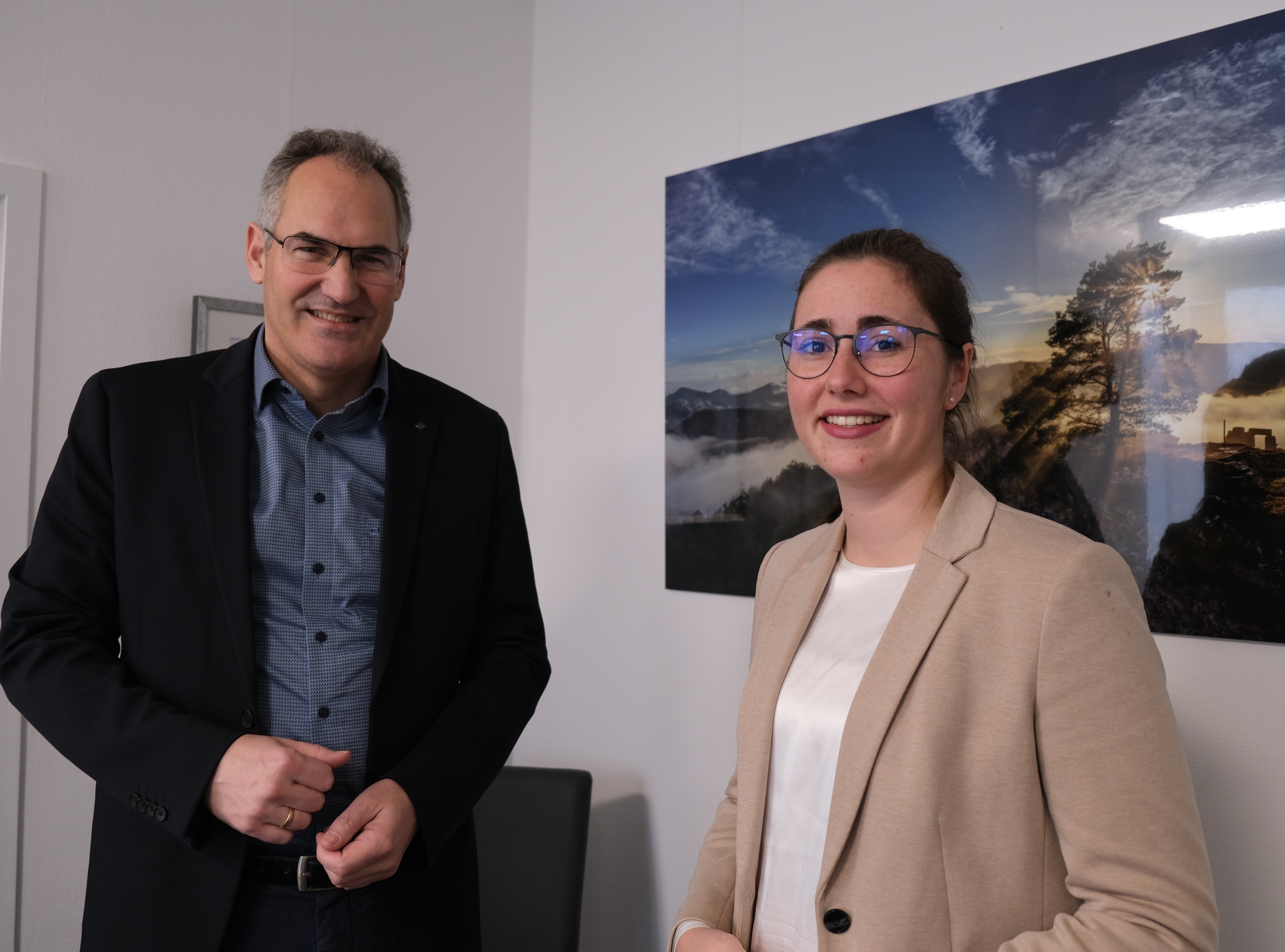 Zwei Personen stehen vor einem Landschaftbiild.