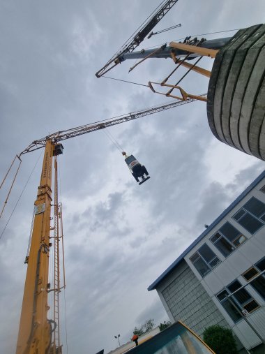 Ein Mini-Bagger hängt an der Seilwinde eines Krans und schwebt über dem Innenhof der Paul-Gillet-Realschule plus in der Edenkobener Luitpoldstraße. Foto: KV SÜW