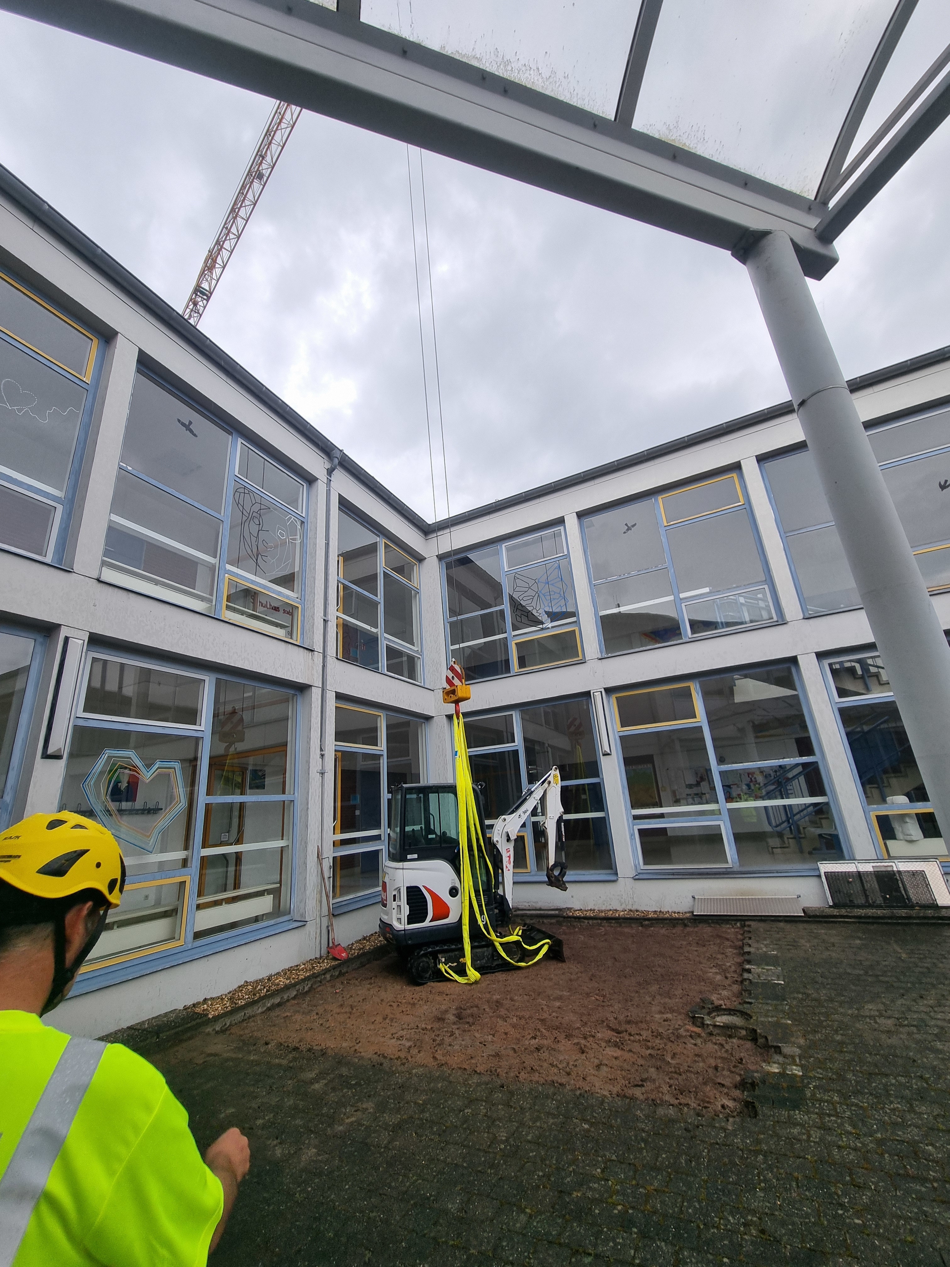 Ein Minibagger steht, noch über eine Seilwinde an einem Kran befestigt, im Innenhof der Paul-Gillet-Realschule plus in Edenkoben.