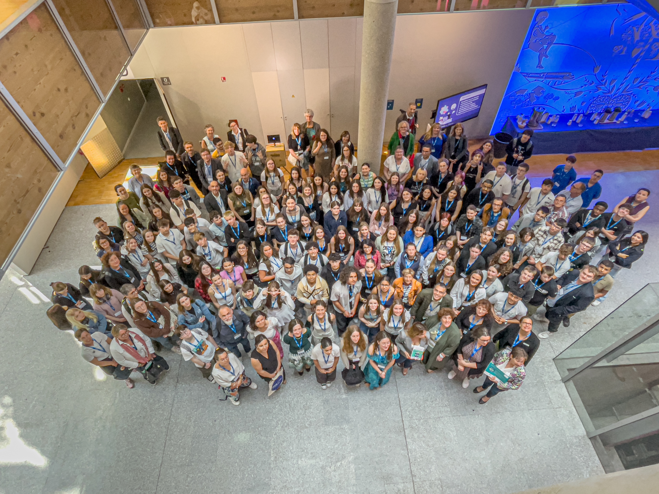 Ein Gruppenfoto der Abschlussveranstaltung von OrienTEE in Straßburg. Die Personen stehen dicht beieinander in einem hellen, modernen Gebäude und blicken nach oben zur Kamera.