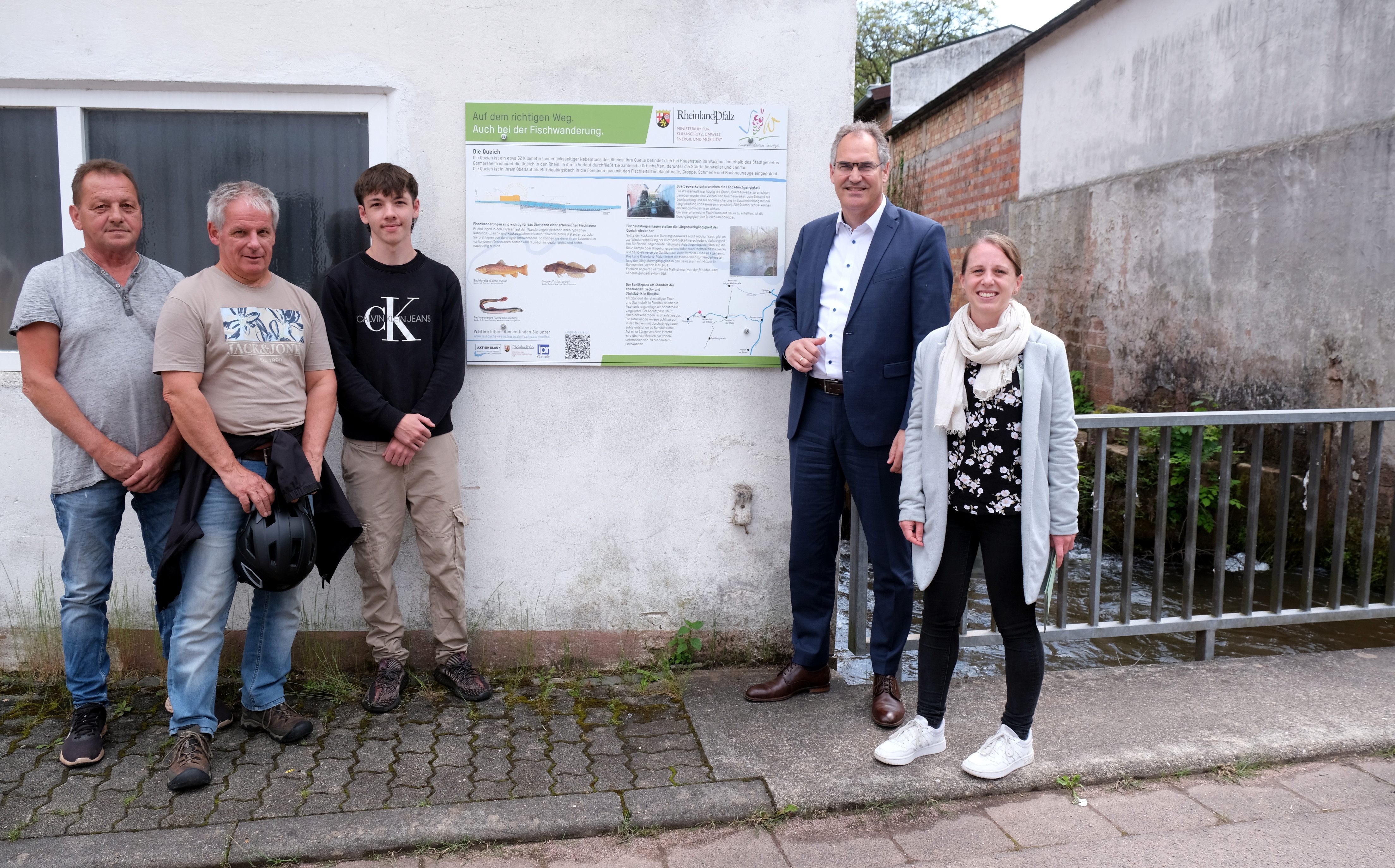 Fünf Personen stehen vor einem weißen Gebäude mit einer Infotafel über den Fischpass in Rinnthal. Von links nach rechts: Johannes Netzer, Werner Schreiner, Darius Netzer, Dietmar Seefeldt und Denise Benzinger. 