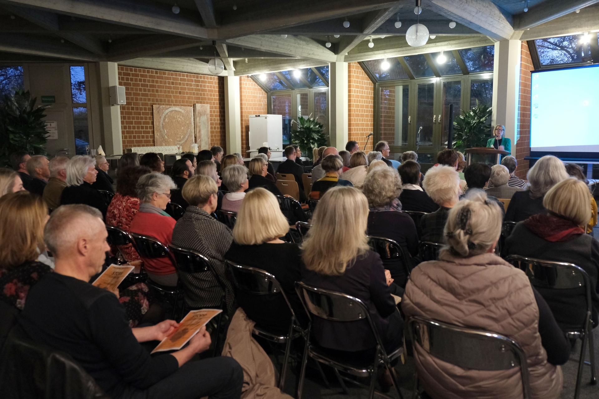 Eine größere Gruppe von Menschen sitzt im Casino der Kreisverwaltung und hört einem Vortrag zu. Im Vordergrund ist das Publikum von hinten zu sehen, während Gleichstellungsbeauftragte Isabelle Stähle am Rednerpult vorne rechts spricht.