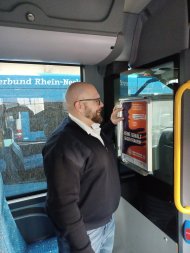 n den Bussen der von der Kreisverwaltung beauftragten Verkehrsunternehmen hängen die Busfahrerinnen und Busfahrer Plakate zum Aktionstag gegen Gewalt an Frauen auf. Foto: VRN Ein Busfahrer befestigt ein Plakat zum Aktionstag gegen Gewalt an Frauen an einer Halterung im Fahrgastraum eines Busses.
