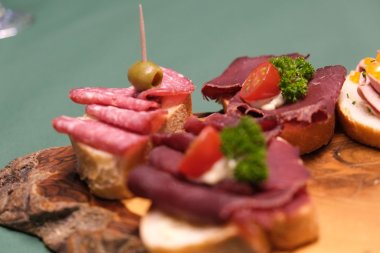 Auch Wildsalami und Wildschinken gibt es aus der Region. Foto: KV SÜW Nahaufnahme von Weißrotscheiben, die mit Wildsalami und Wildschinken belegt sind. Die Schnittchen liegen auf einer rustikalen Holzplatte.